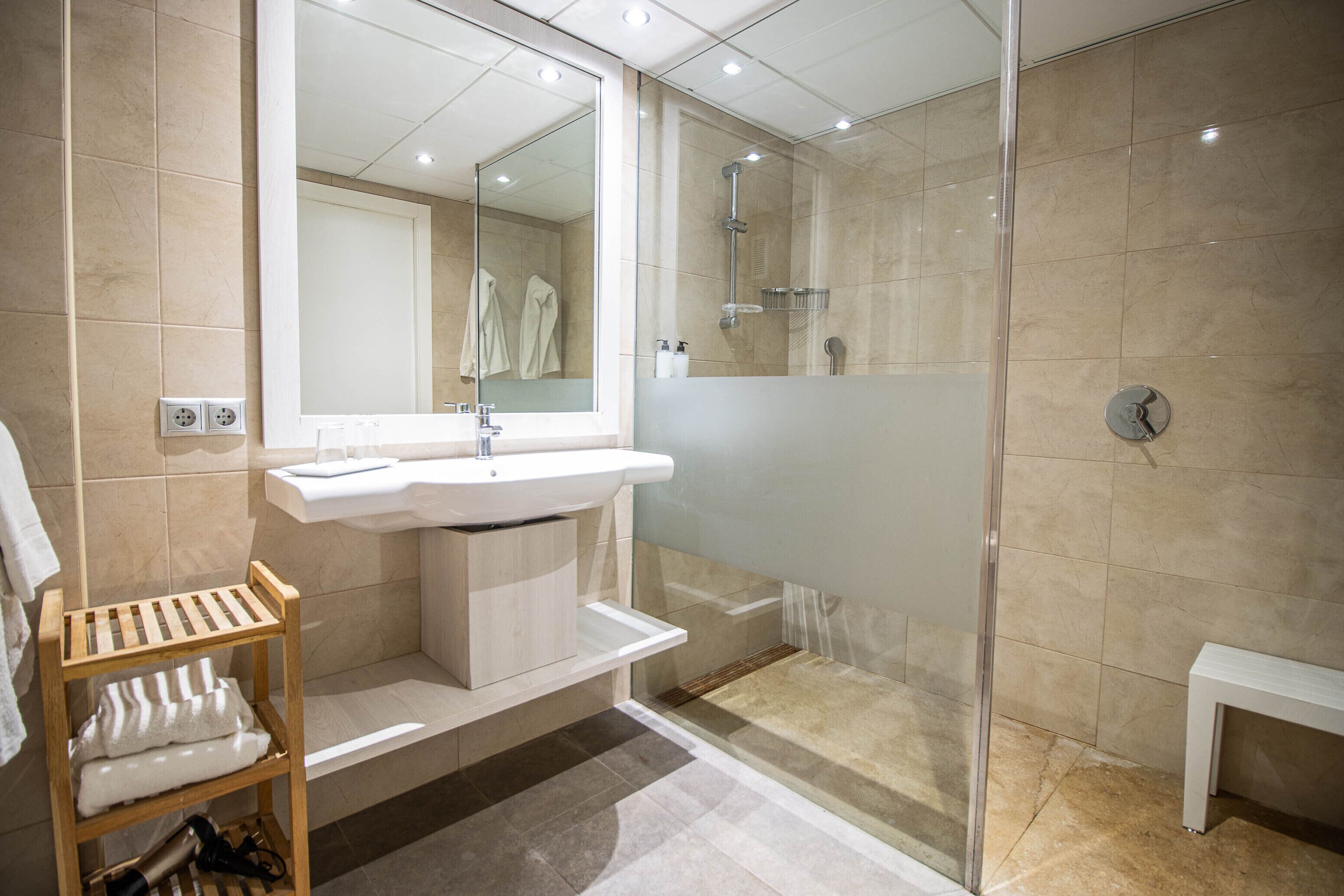 Une salle de bain moderne avec une douche à parois de verre, un lavabo et une étagère en bois où sont posées des serviettes.