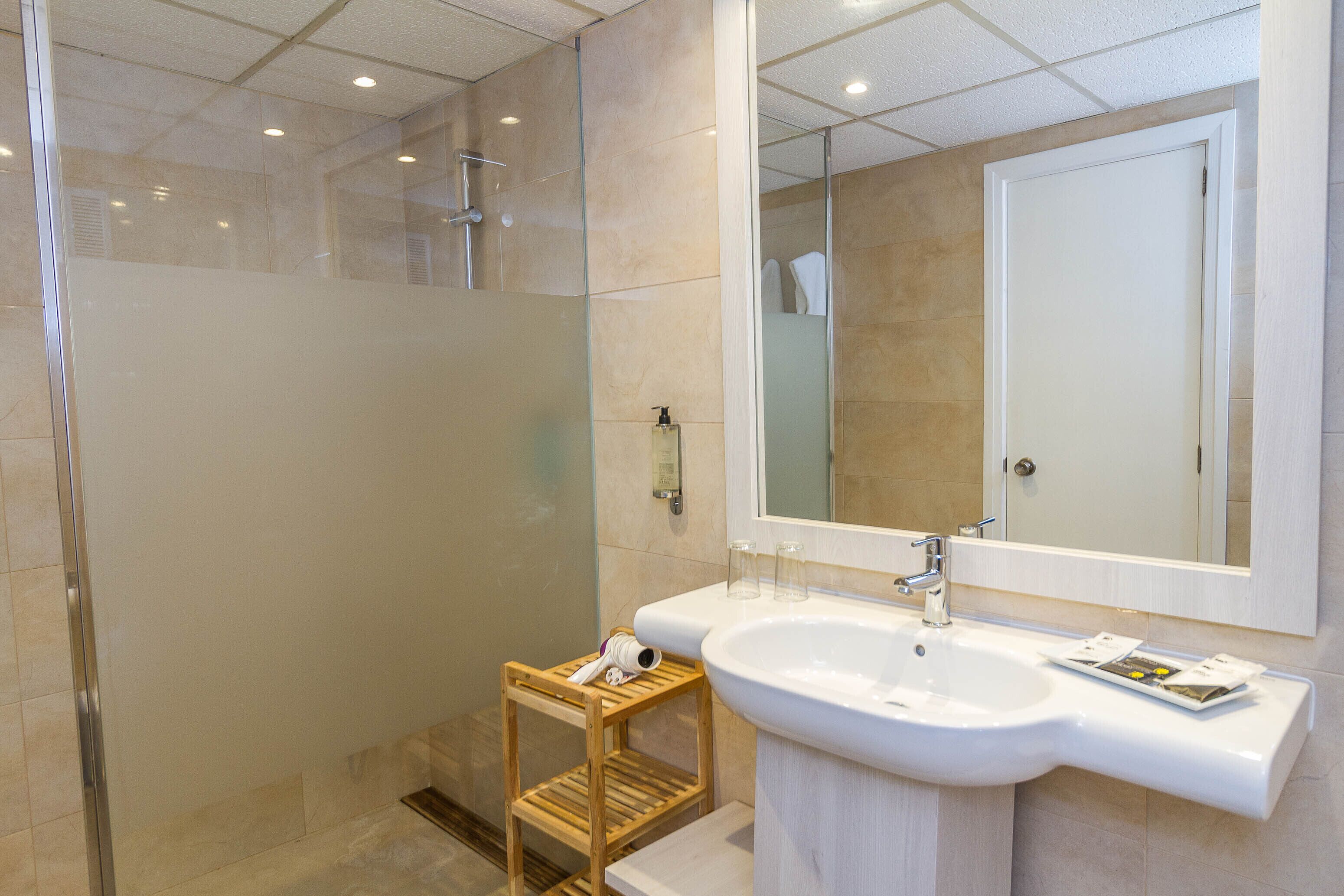 A modern bathroom with a glass-enclosed shower, a wooden stool, a white sink, and a mirror above it.