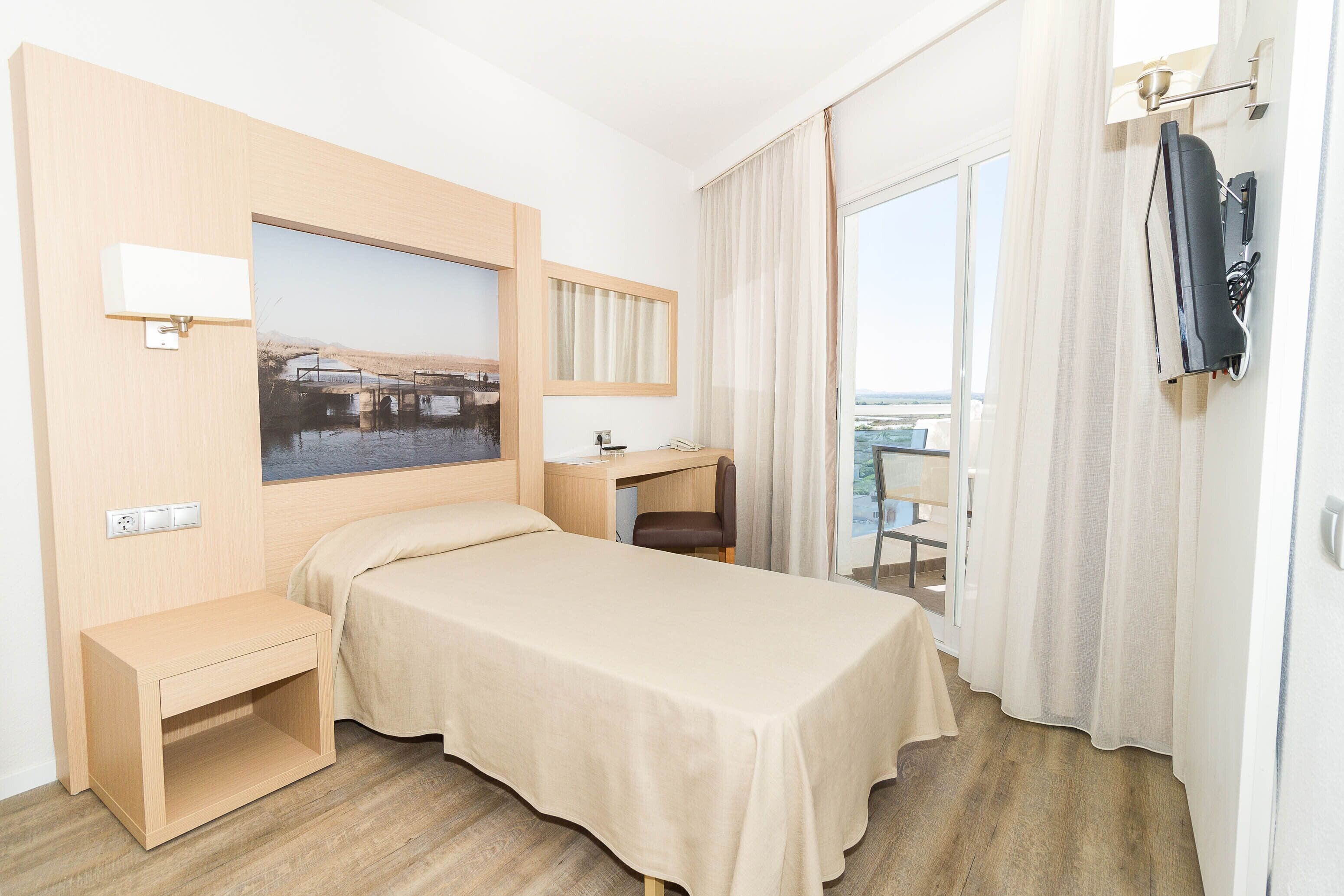 A hotel room with a bed, a desk, a chair, a TV, and a window with curtains.