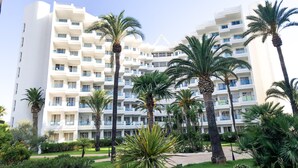 Un hotel de varios pisos con balcones, rodeado de palmeras y follaje.