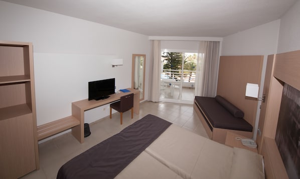 Habitación de hotel con cama, escritorio con televisor, una mesita pequeña y vista al balcón exterior.