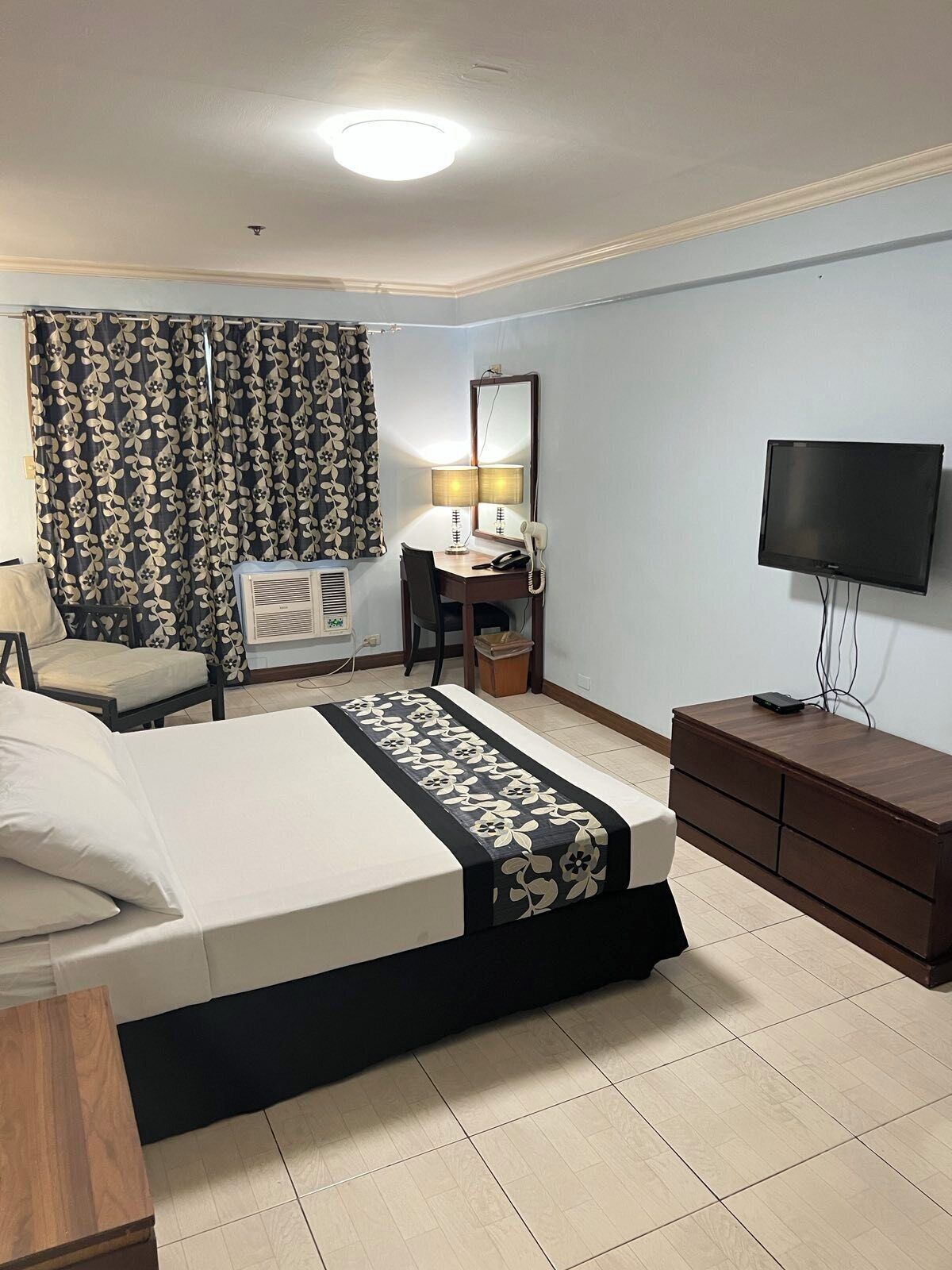 A hotel room with a bed, a desk with a chair, a television, and a dresser.