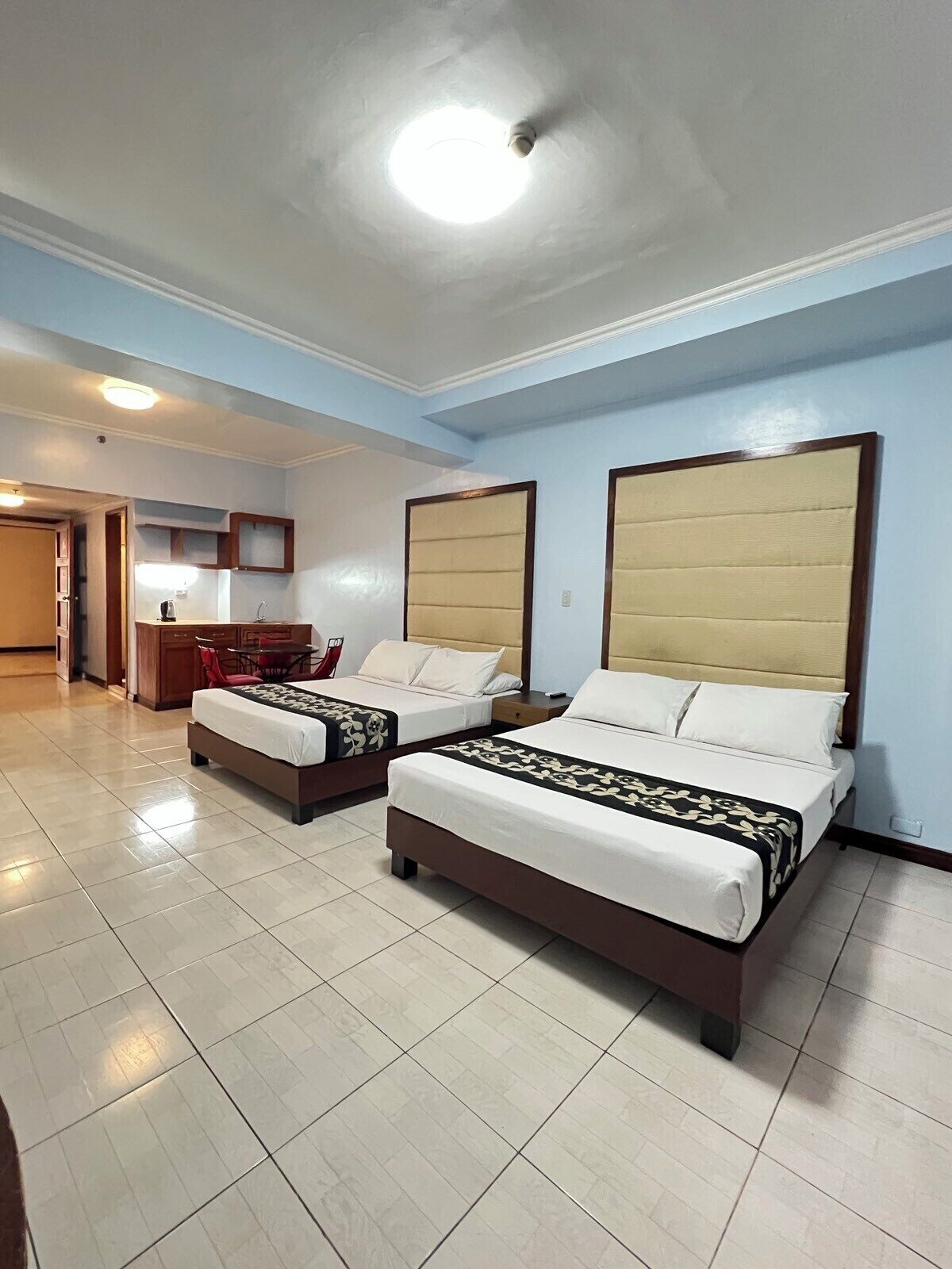 A hotel room with two beds, a small kitchenette, and a bathroom.