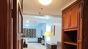 A hallway with a wooden cabinet, a lamp, and a patterned curtain. - Jupiter Suites (Makati)