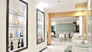 A hotel corridor with a glass display case on the left, a dining area with checkered tablecloths on the right, and a television mounted on the wall. - Jupiter Suites (Makati)