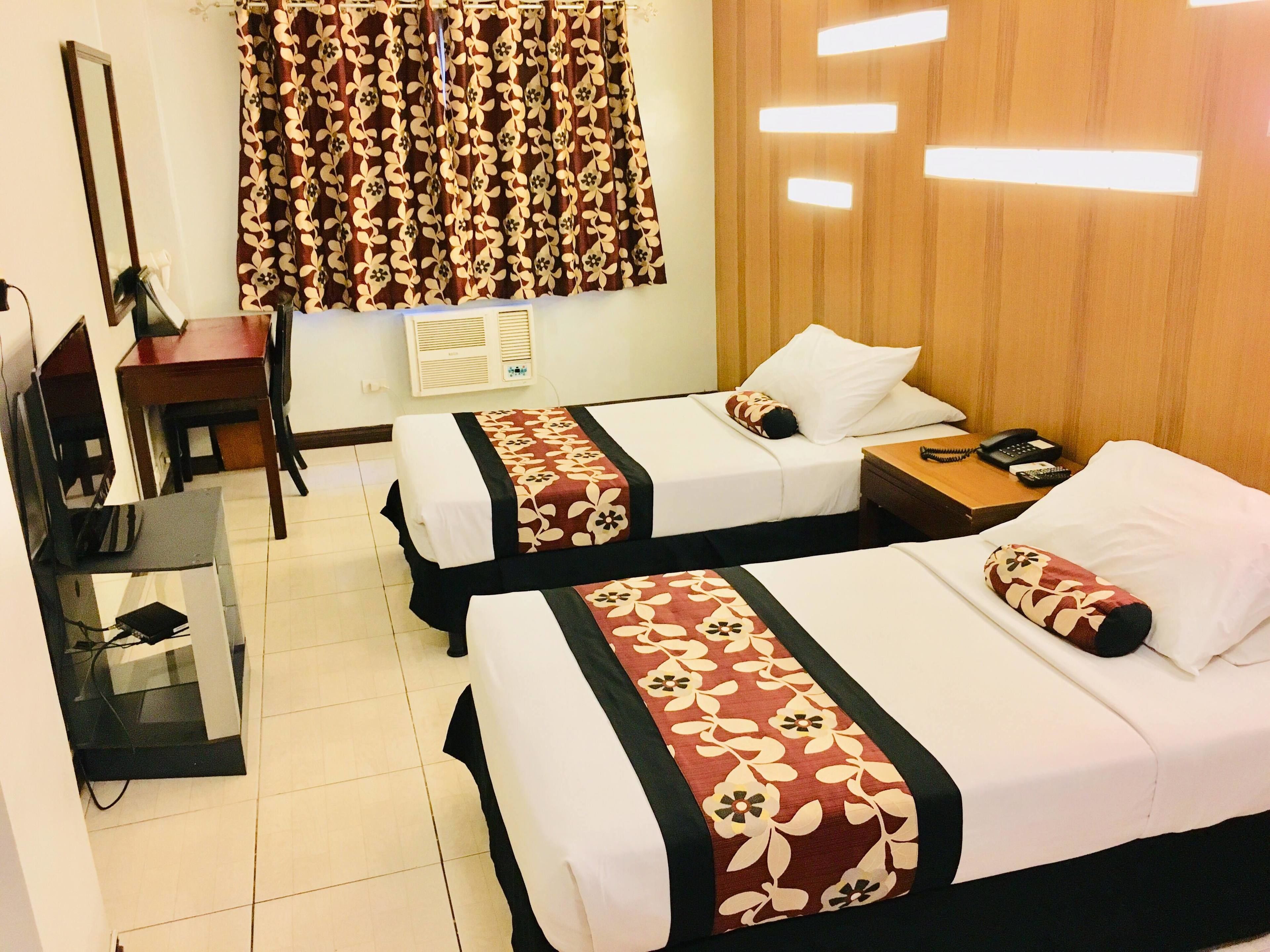 Une chambre d’hôtel avec deux lits, un bureau avec une chaise, une télévision et une fenêtre avec des rideaux.