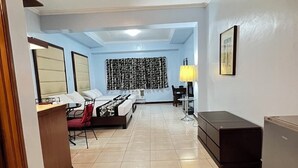 A hotel room with a bed, a desk, a chair, a lamp, and a small table. - Jupiter Suites (Makati)