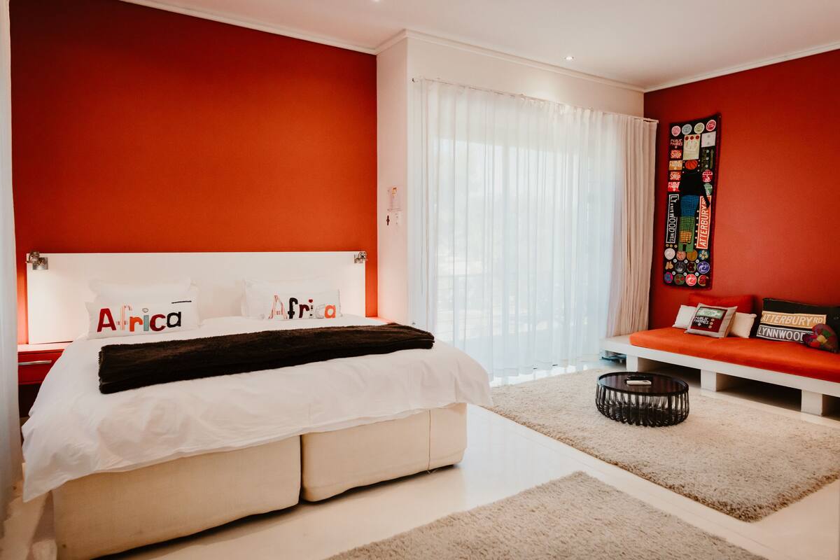 A modern bedroom with a large bed, a white headboard, and a red accent wall.