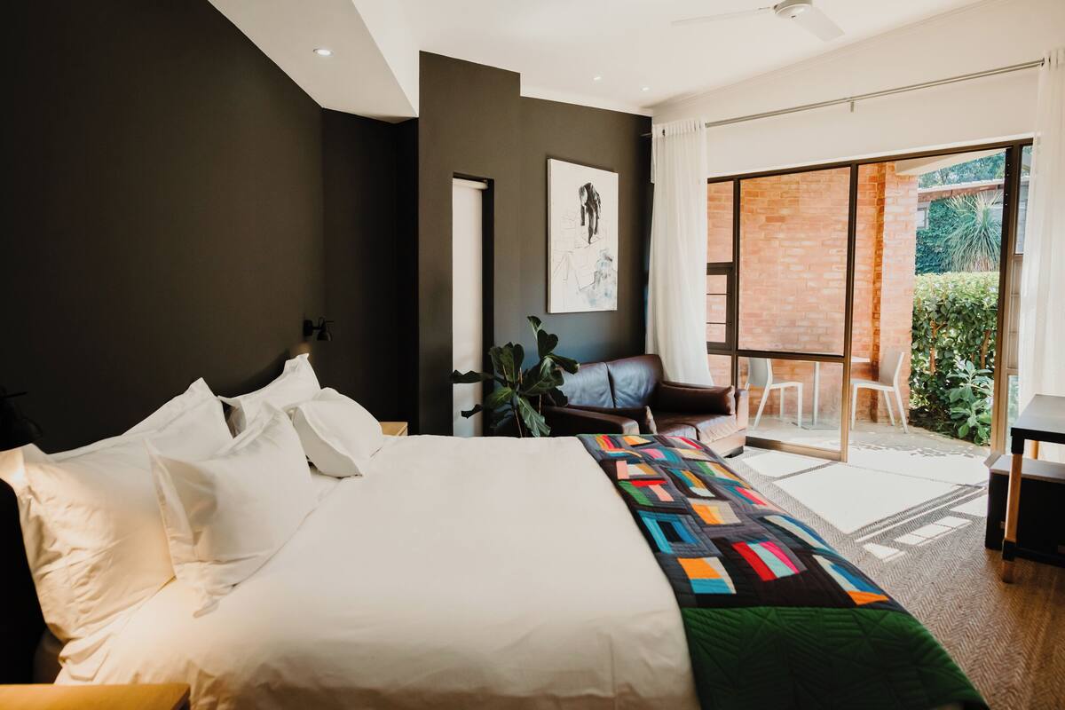 A modern bedroom with a large bed, a view of the outdoors, and a small seating area.