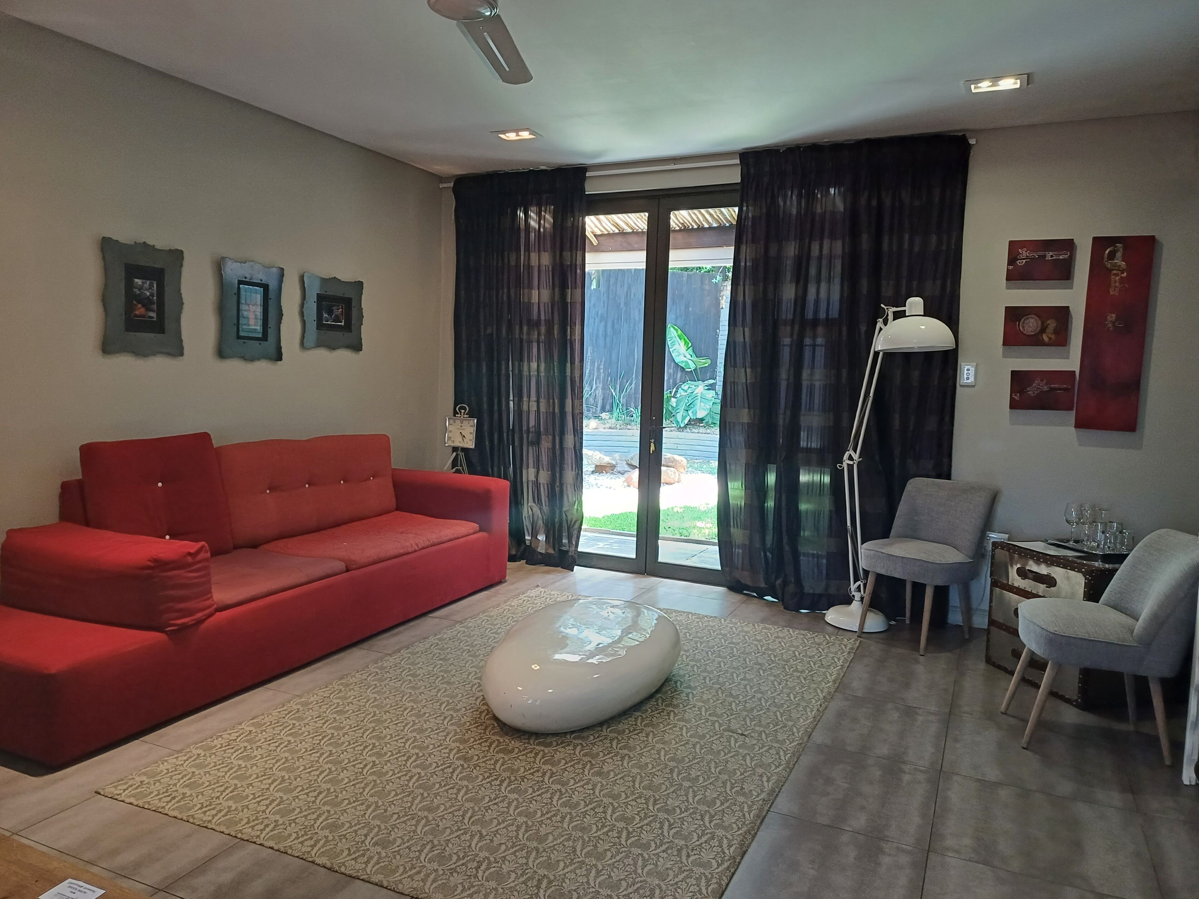 A living room with a red sofa, a white ottoman, a grey armchair, a floor lamp, and a small table with glasses.