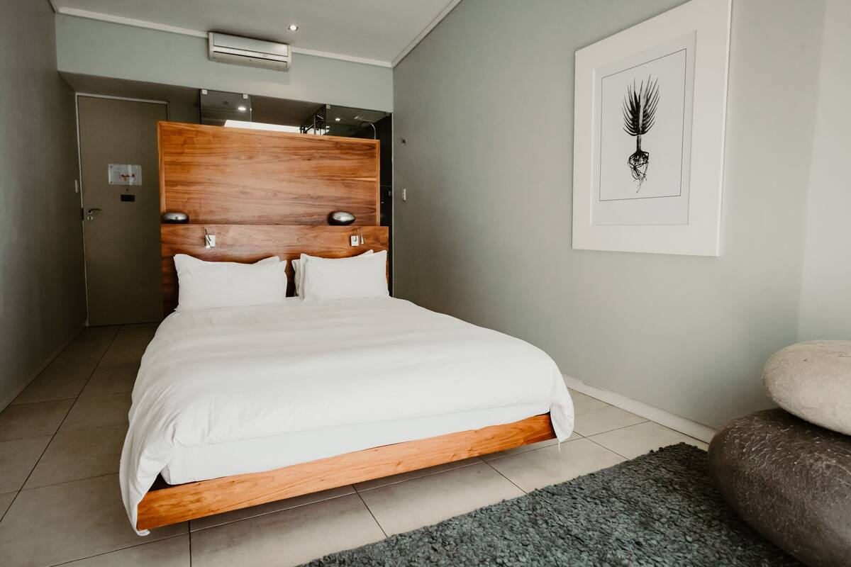 A modern bedroom with a wooden headboard, a large bed, a gray rug, and a framed artwork on the wall.