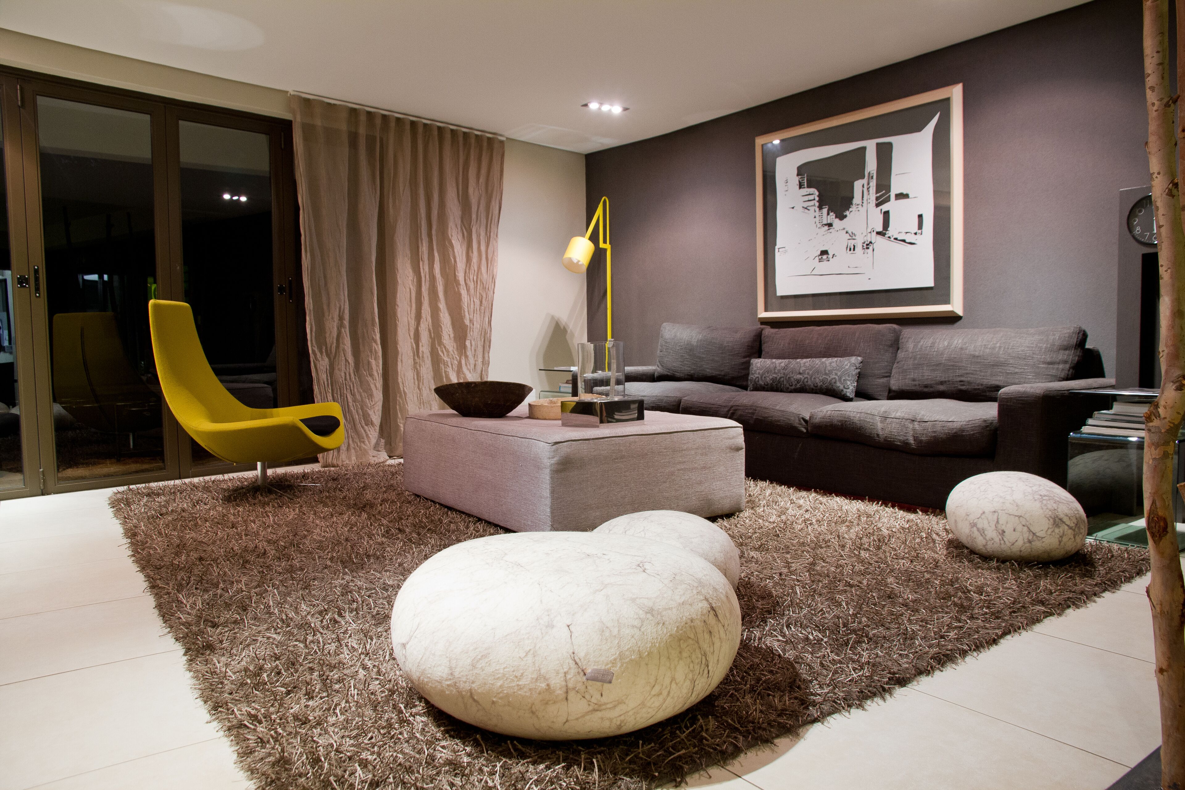 A modern living room with a sofa, ottoman, and a yellow chair.