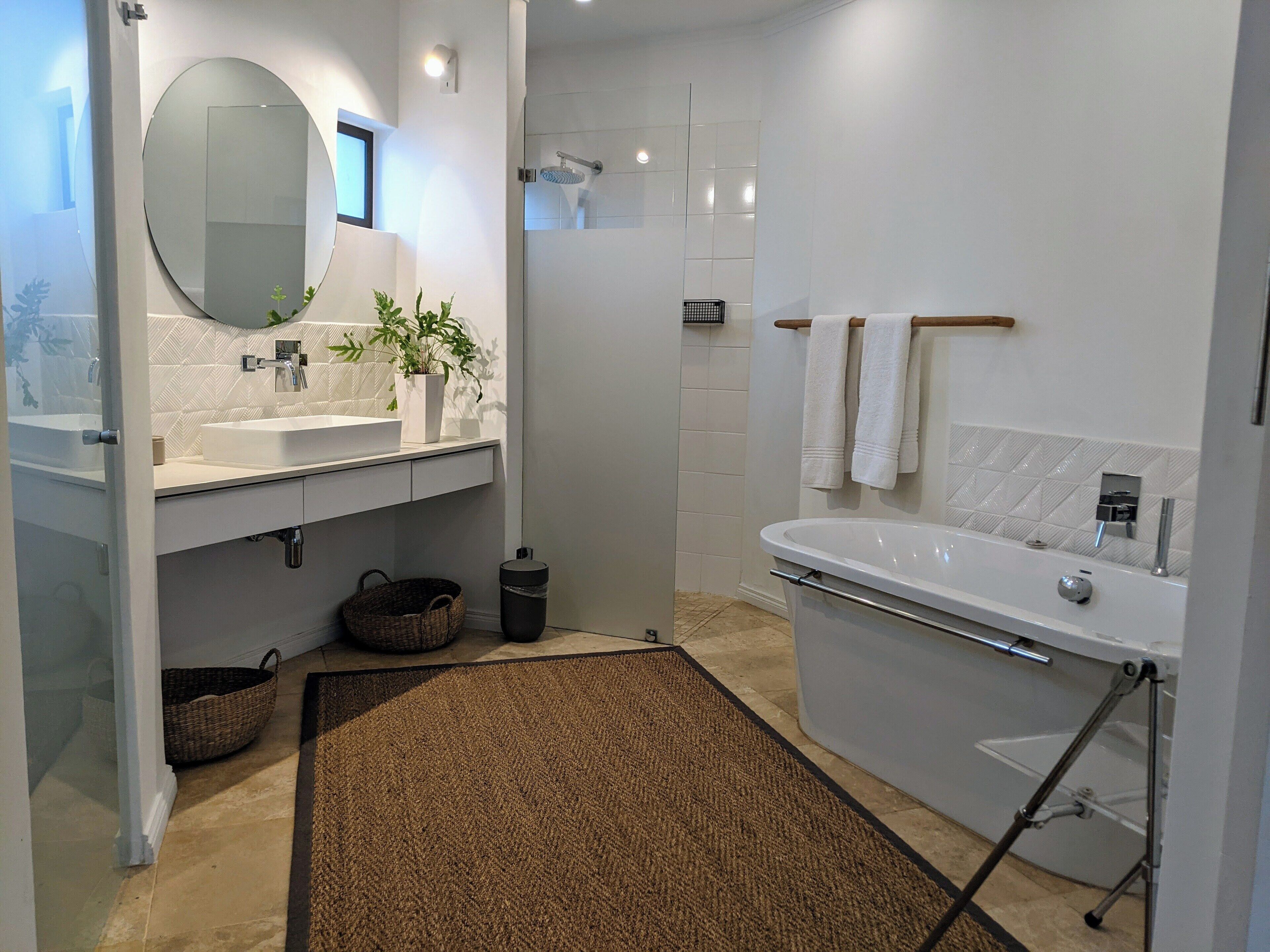 Une salle de bain moderne avec un grand miroir, un lavabo et une douche. Des serviettes sont suspendues sur un porte-serviettes et une plante en pot est posée sur le comptoir.