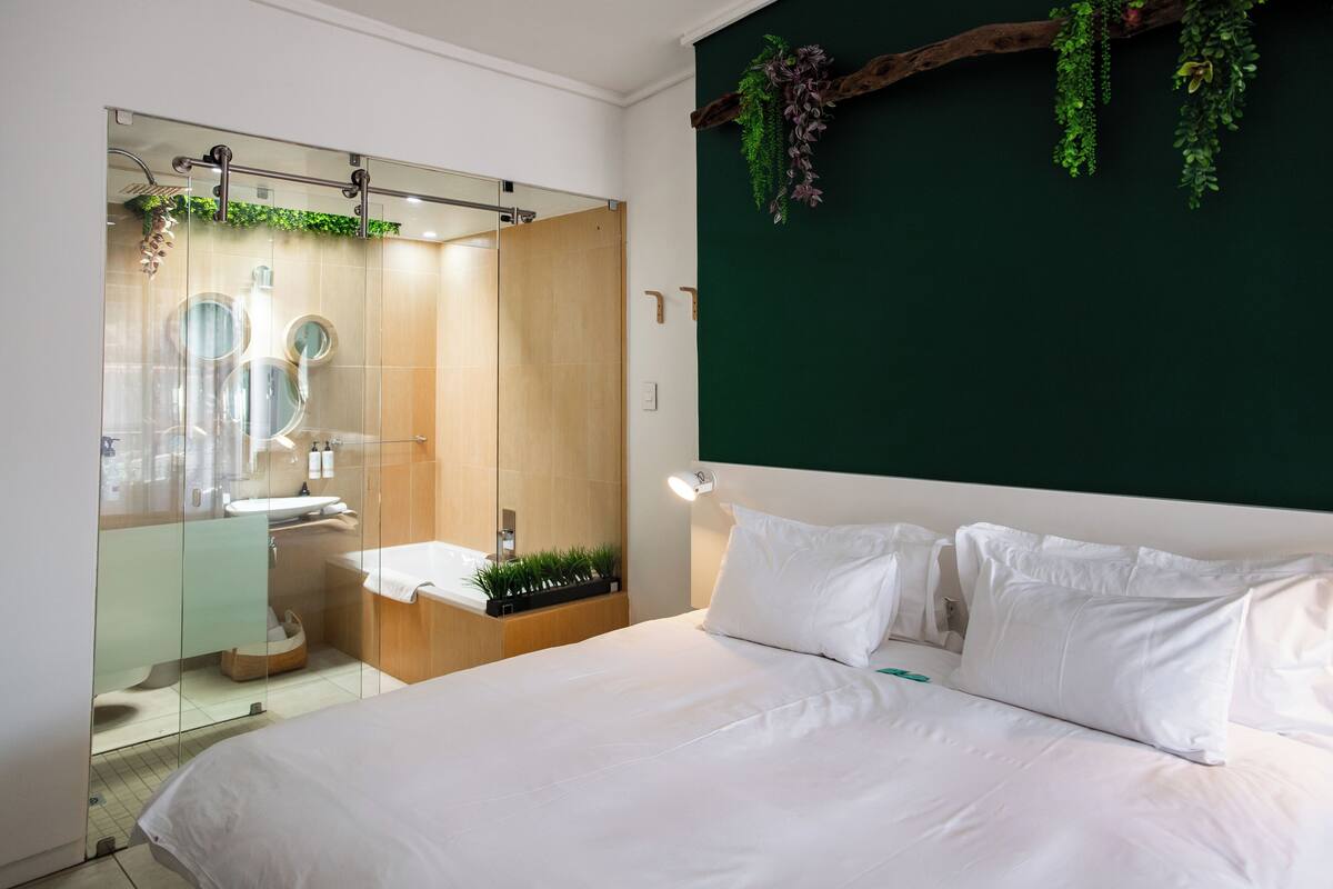 A modern hotel room with a large bed, a glass-enclosed shower, and a green accent wall.