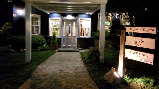 A well-lit entrance with a stone pathway leading to a building with a sign indicating "Hosteria" and "La Casa de Eugenia." - Hosteria La Casa de Eugenia (San Martín de los Andes)