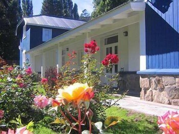 Una casa con porche, rodeada por un jardín lleno de flores.
