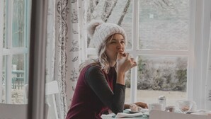 A person sitting at a table with a window view, a cup, and a plate with food. - Hosteria La Casa de Eugenia (San Martín de los Andes)