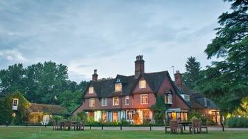 A large, traditional brick house with multiple chimneys, surrounded by a well-maintained lawn and trees.