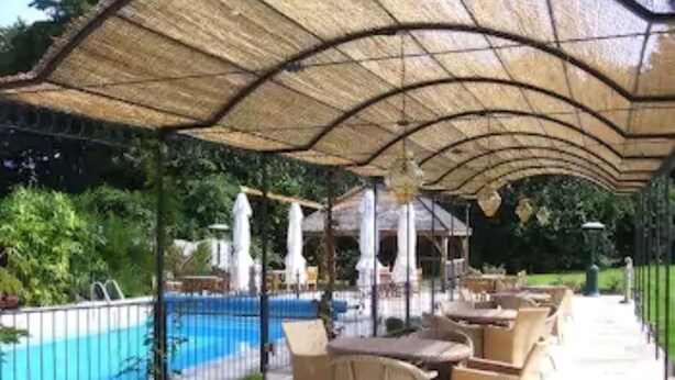 An outdoor pool area with a covered patio, lounge chairs, and a fence. - Ravenwood Hall Hotel (Bury St Edmunds)