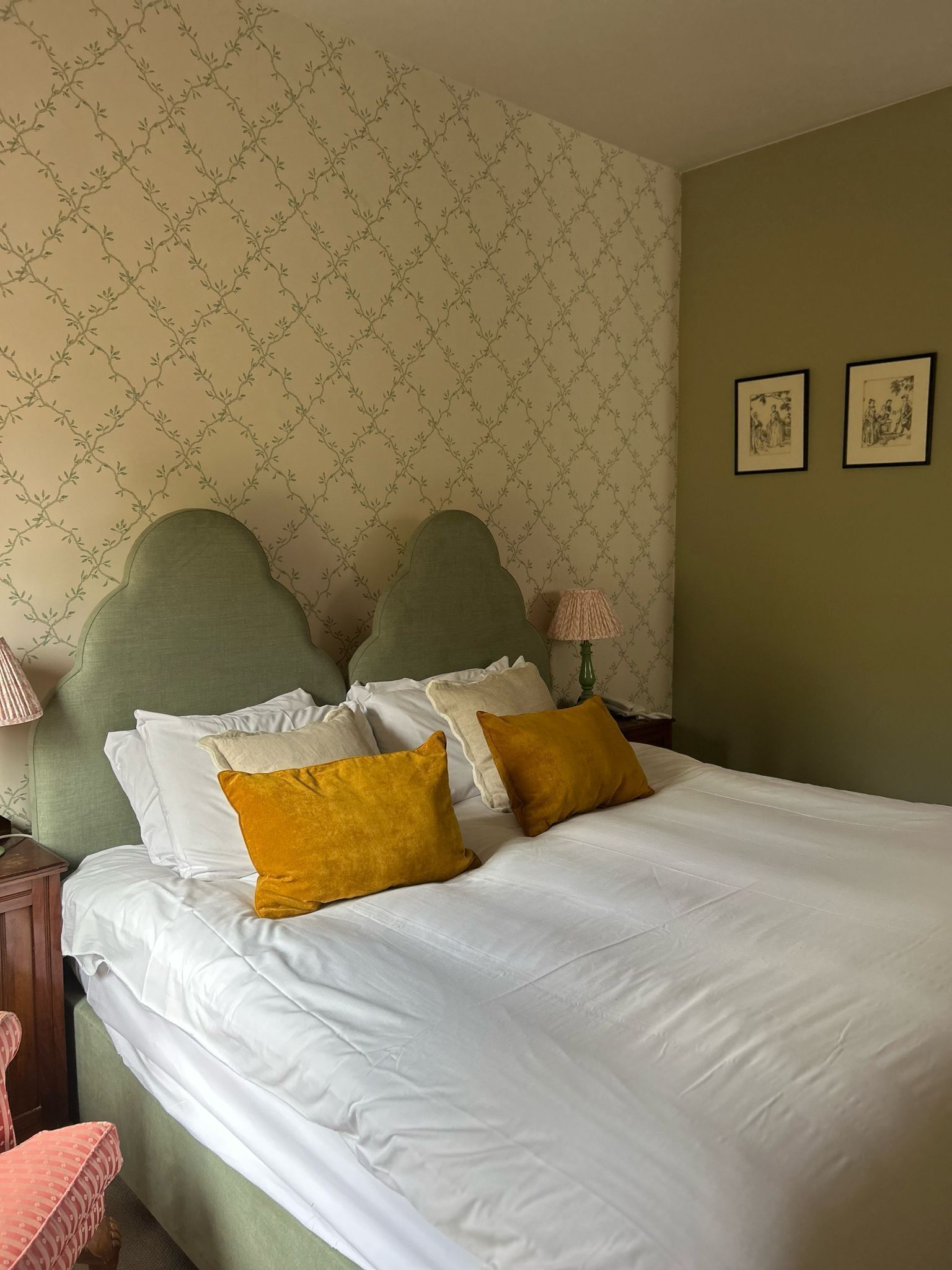 A neatly made bed with white and mustard pillows, a green headboard, and a patterned wallpaper.