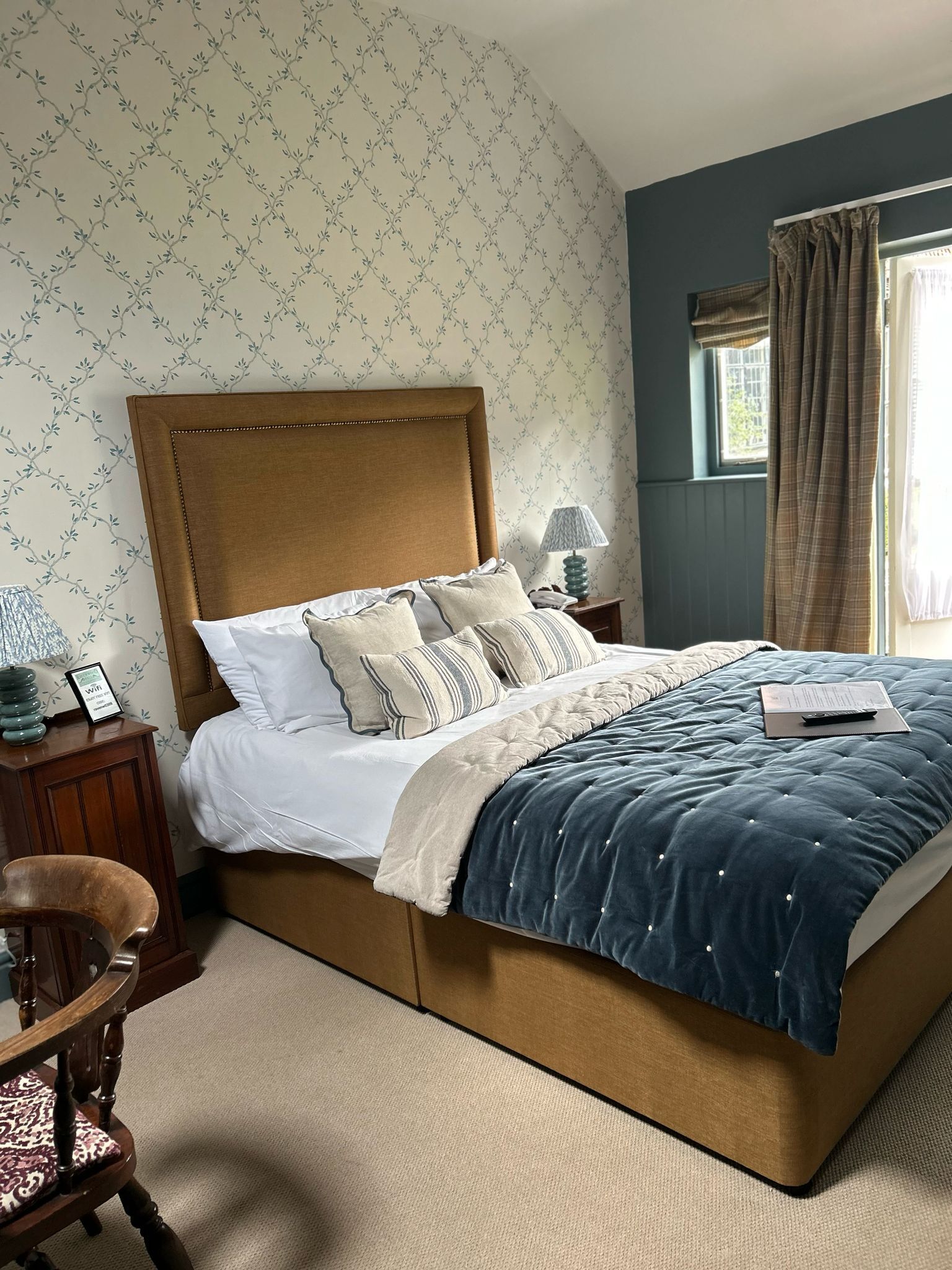A bedroom with a large bed, a wooden nightstand, a chair, and a window with curtains.