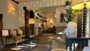 A cozy hotel lobby with a fireplace, plush seating, and a dining area. - Ravenwood Hall Hotel (Bury St Edmunds)