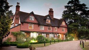 A large, traditional brick house with multiple chimneys, a well-maintained garden, and a gravel driveway. - Ravenwood Hall Hotel (Bury St Edmunds)