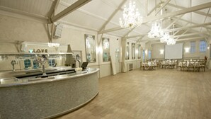 A spacious room with a curved reception desk, chandeliers, and a large mirror. - Ravenwood Hall Hotel (Bury St Edmunds)