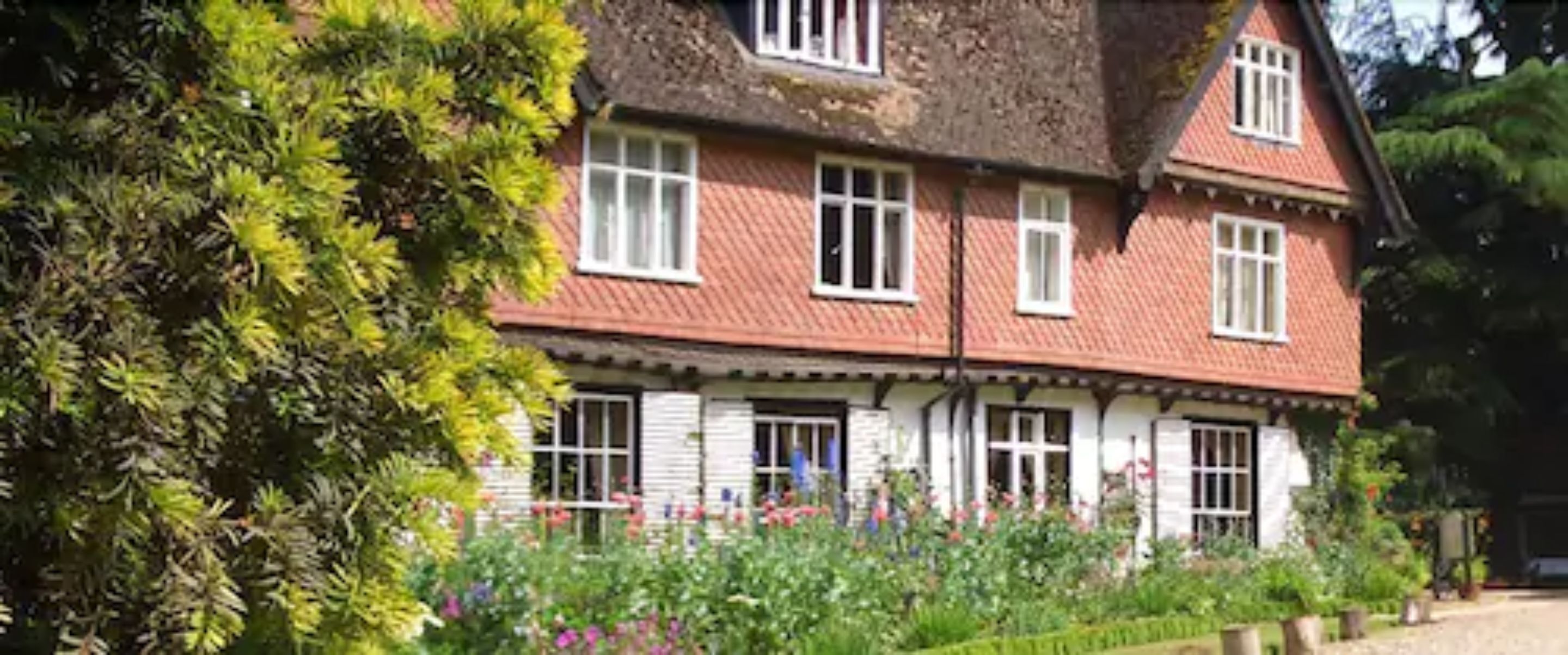 A traditional two-story house with a red-tiled roof, white-framed windows, and a well-maintained garden with various plants and flowers.