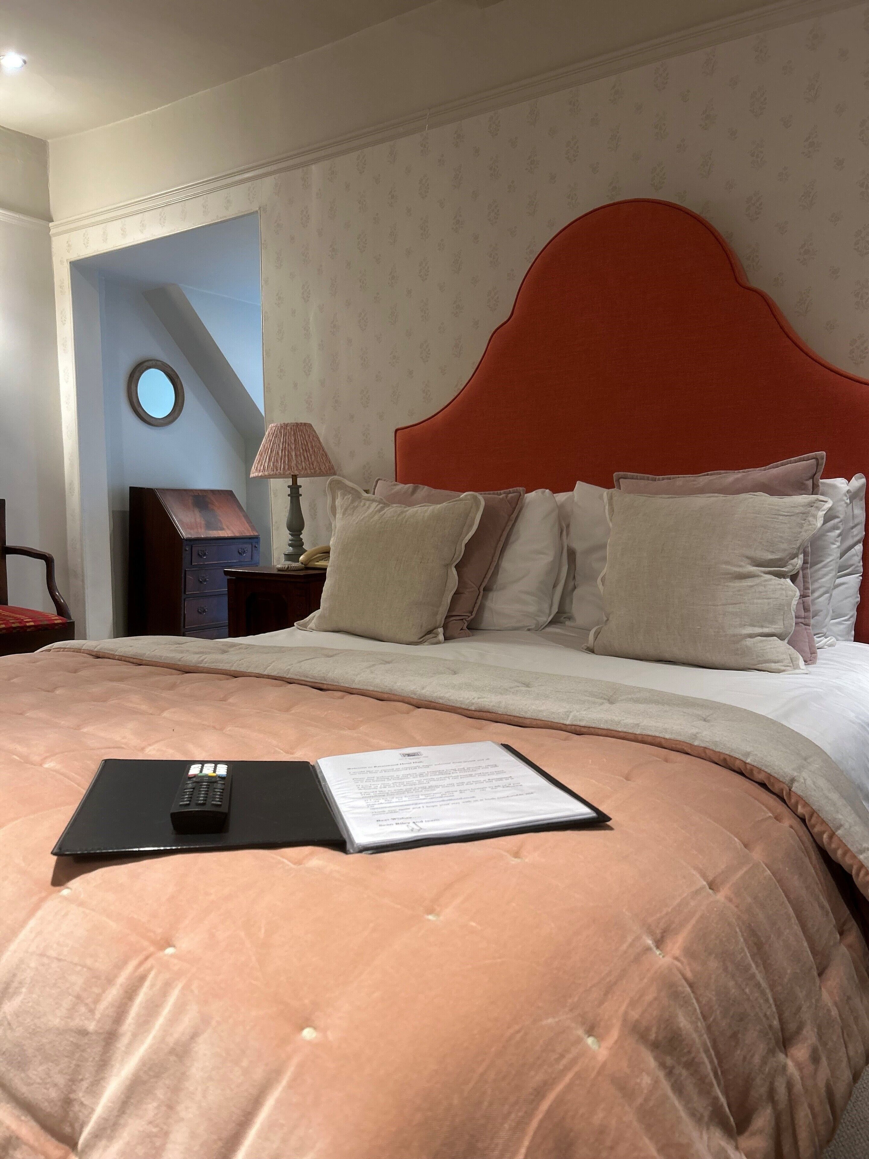 A neatly made bed with a red headboard, a bedside table with a lamp, and a mirror on the wall.