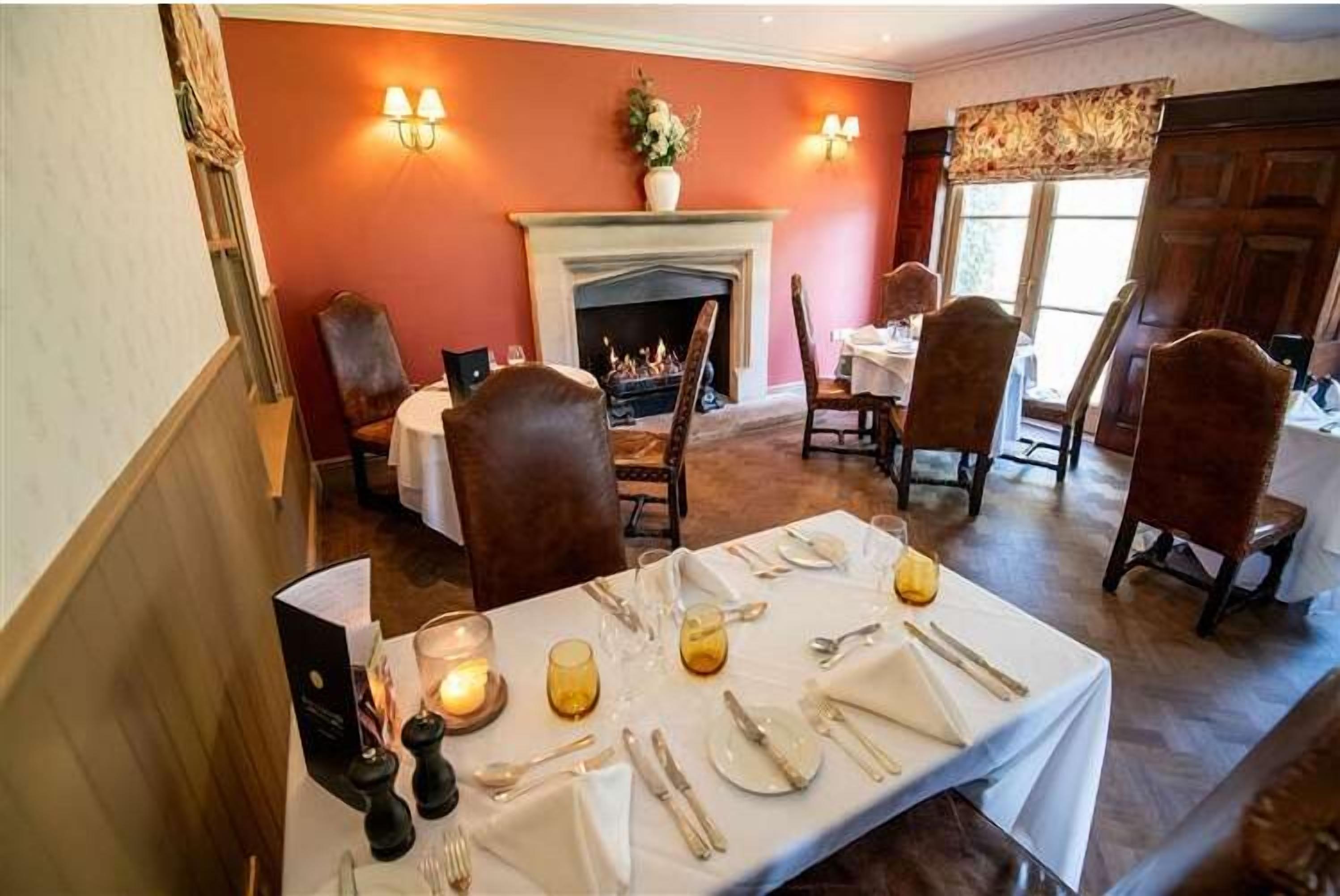 Une salle à manger avec une cheminée, des chaises en bois, une table dressée pour quatre personnes et une vue sur l’espace repas.