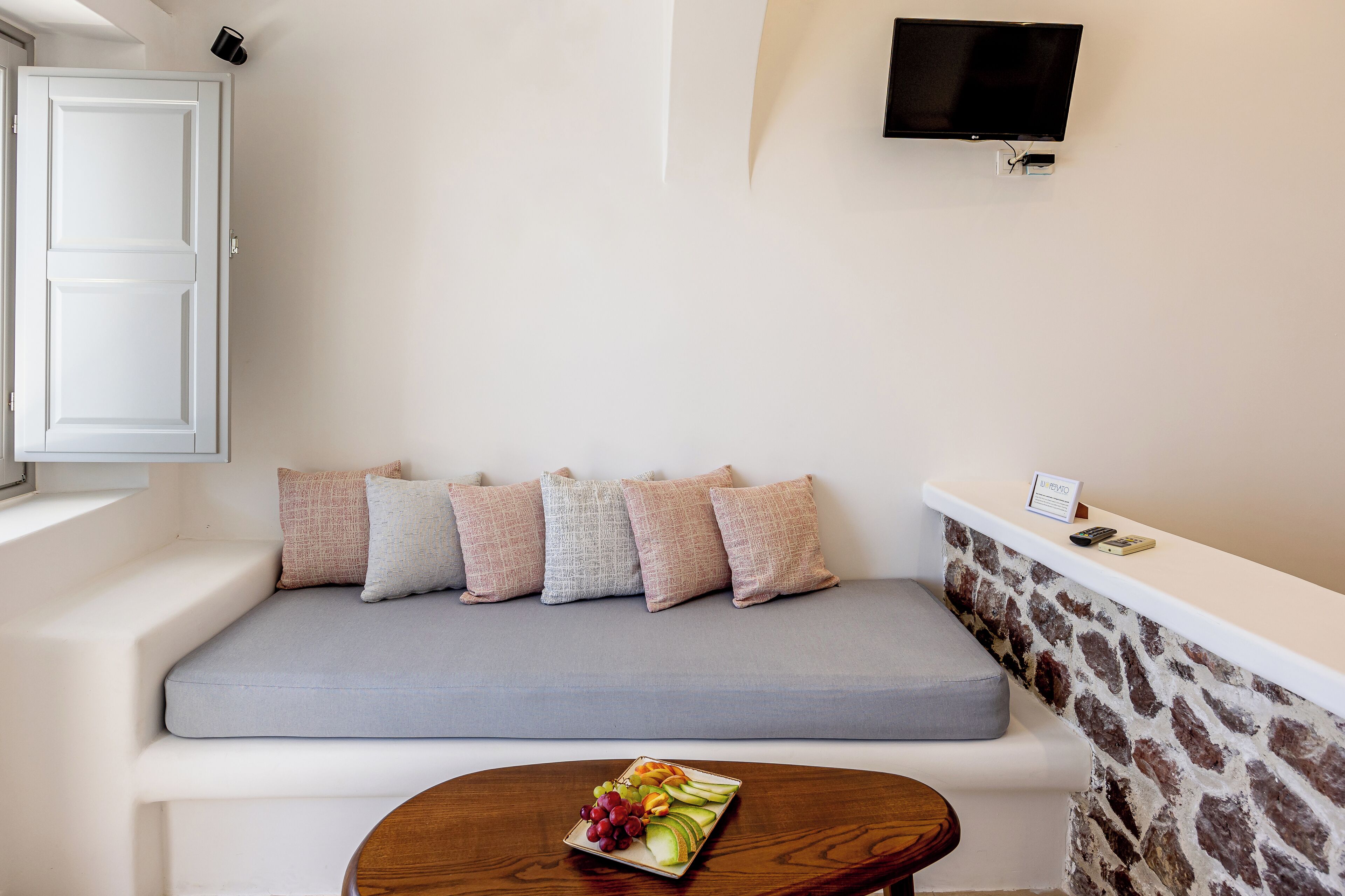 A room with a grey sofa, a stone wall, a flat-screen TV, and a small table with fruit.