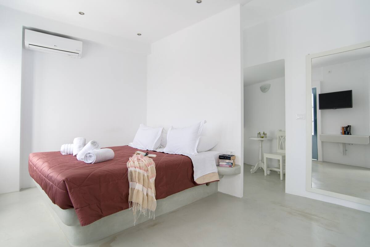 A modern hotel room with a bed, a TV, a small table, and a mirror.