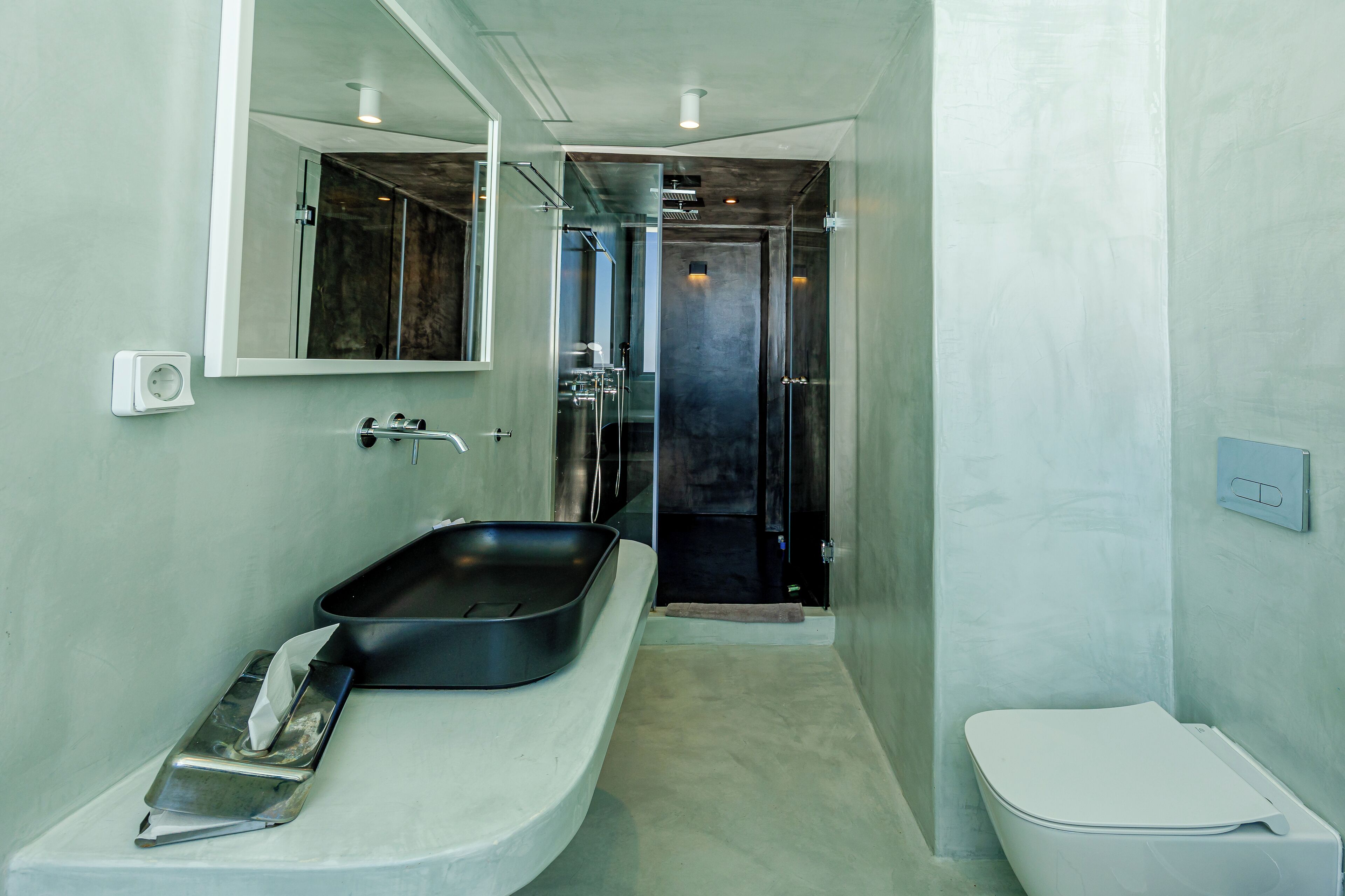 A bathroom with a large mirror, a black sink, a white toilet, and a shower area.