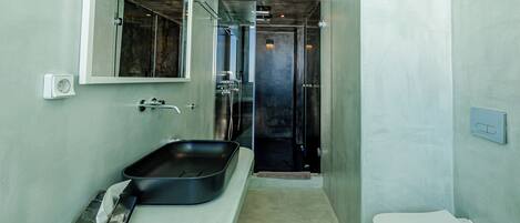 A bathroom with a large mirror, a black sink, a white toilet, and a shower area.