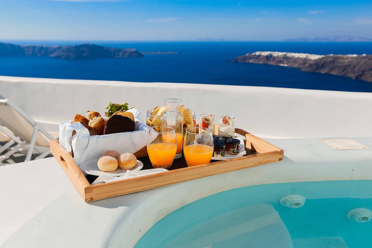 A breakfast tray with pastries, juice, and coffee on a balcony overlooking the sea.