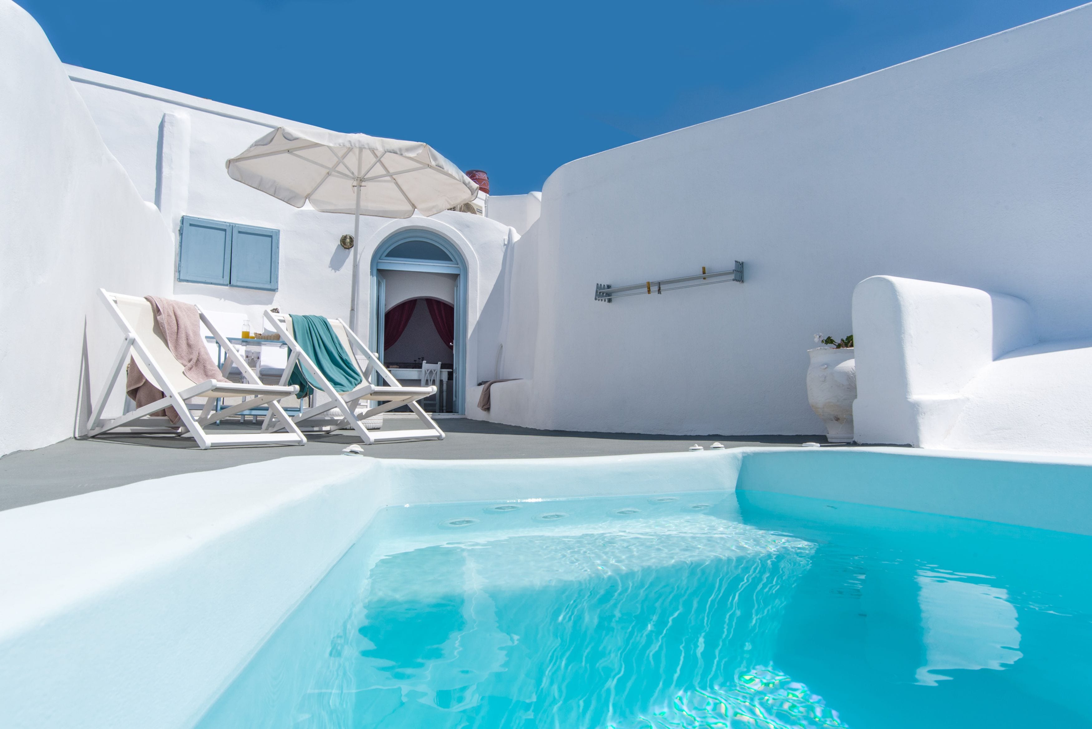 A white-walled pool area with lounge chairs and an umbrella.