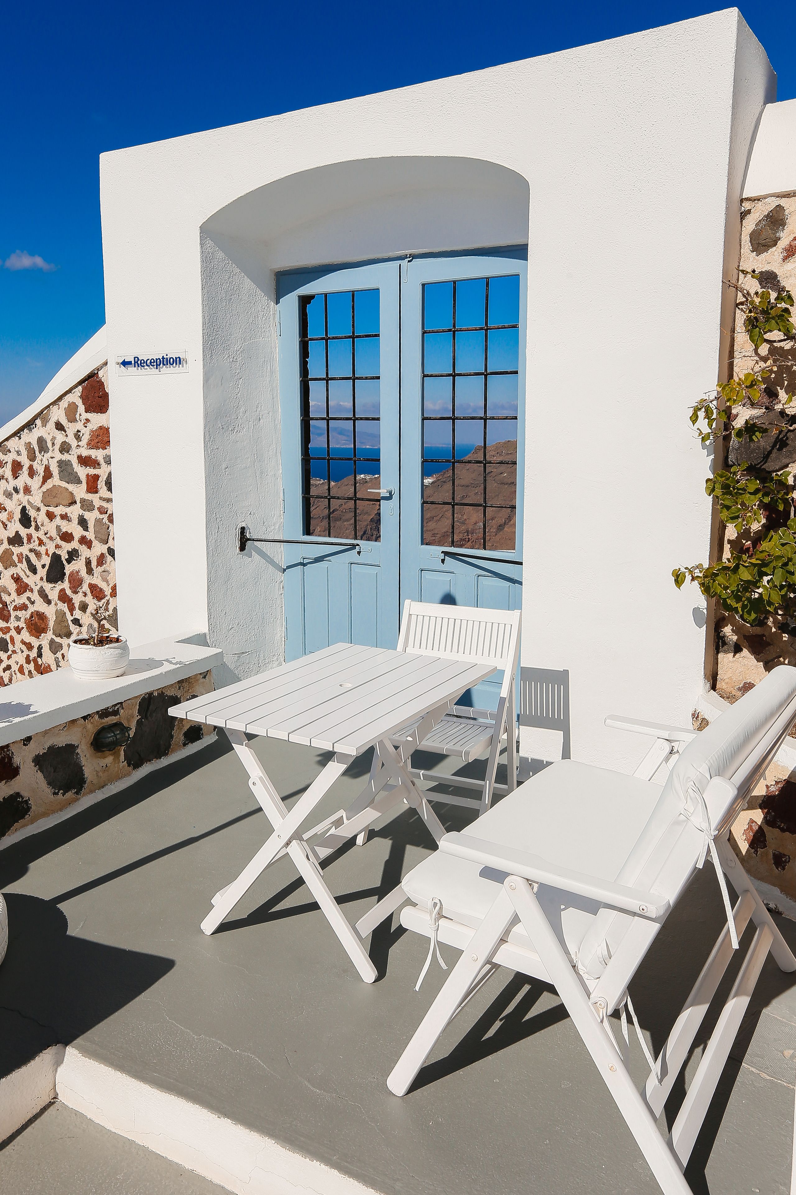 A white building with a reception sign, a blue door, and a view of the sea.