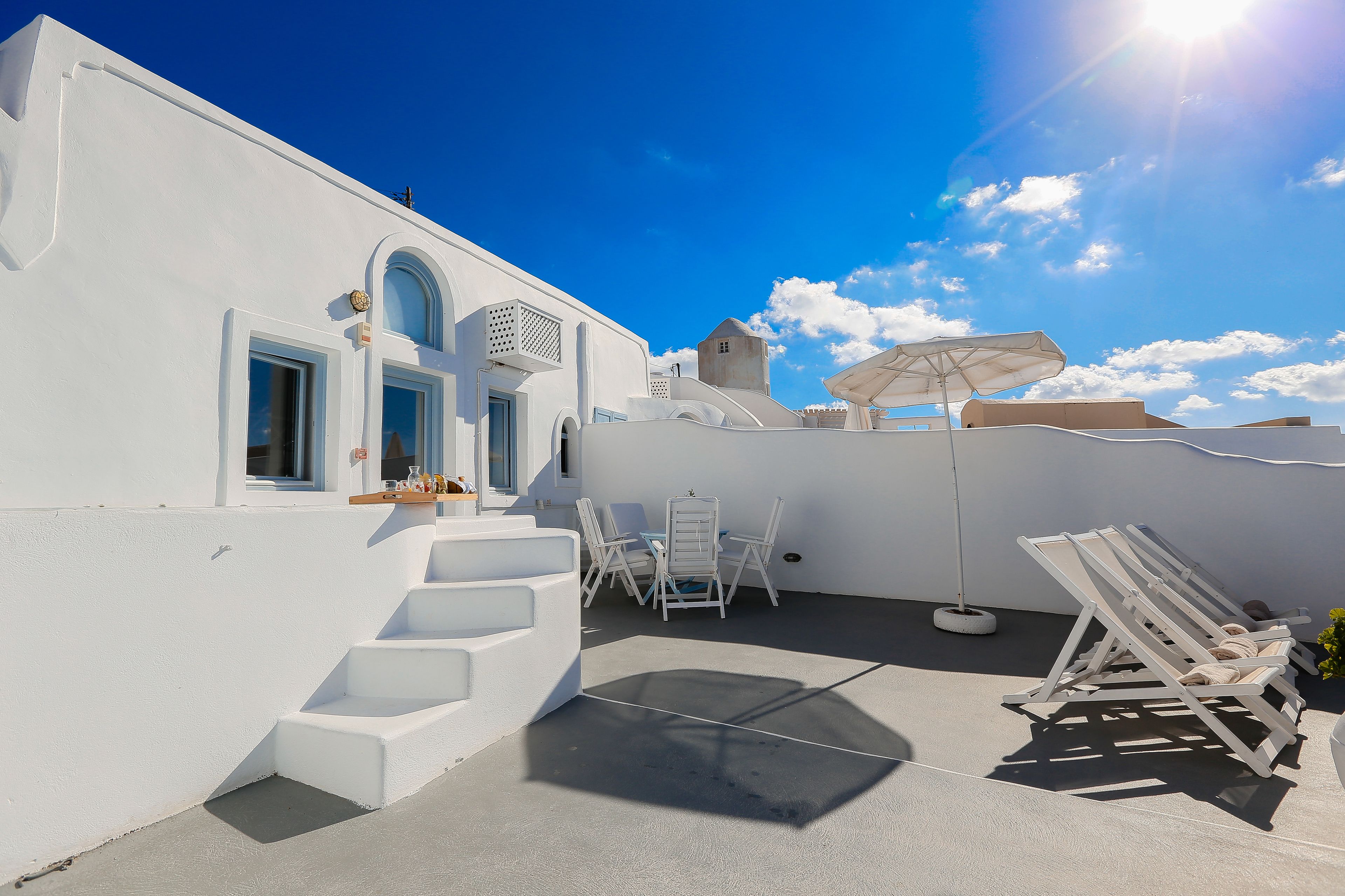 A white building with a terrace, outdoor seating, and a sunshade.