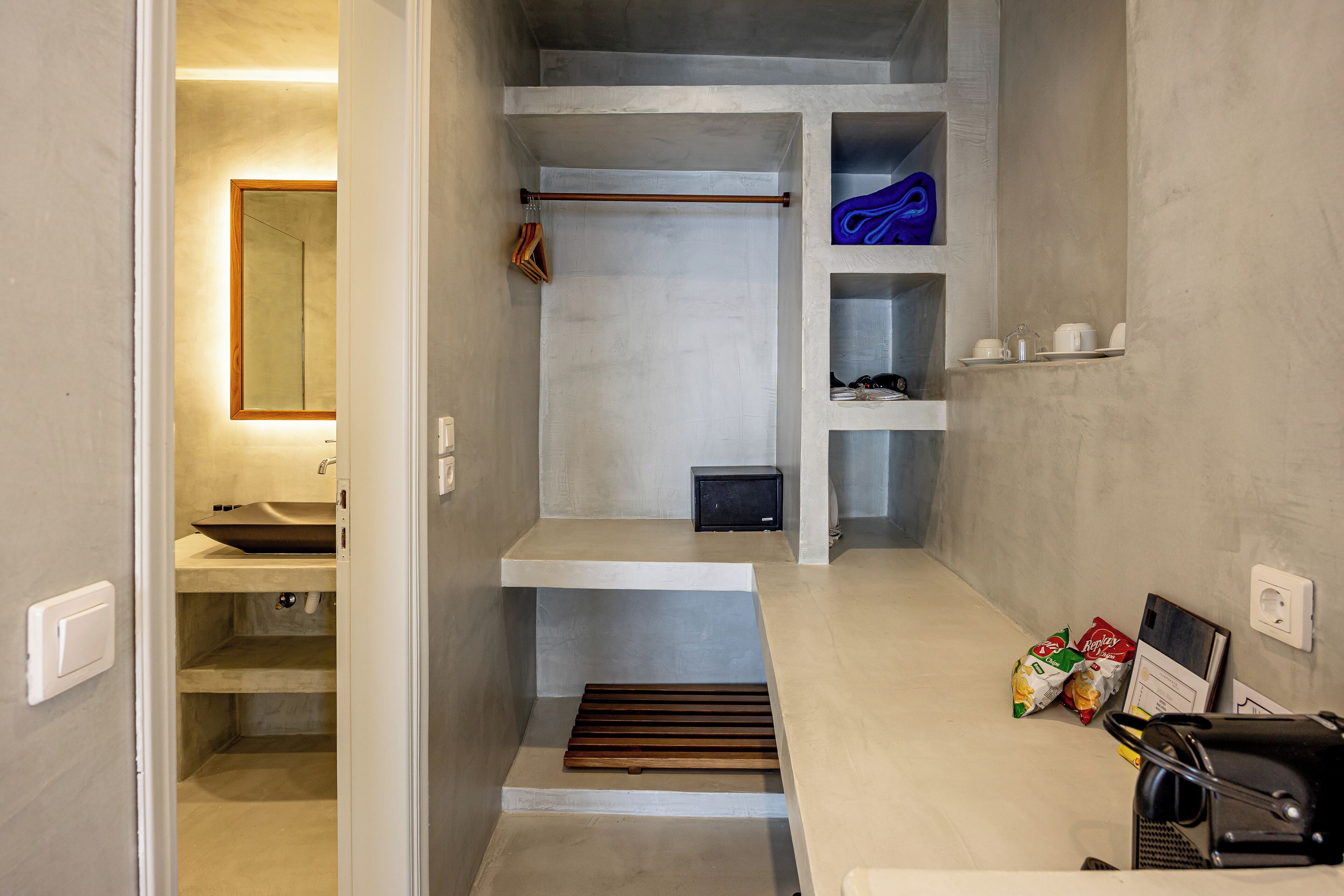 Un baño pequeño con lavamanos, espejo, toallero, estantes y zona de ducha.