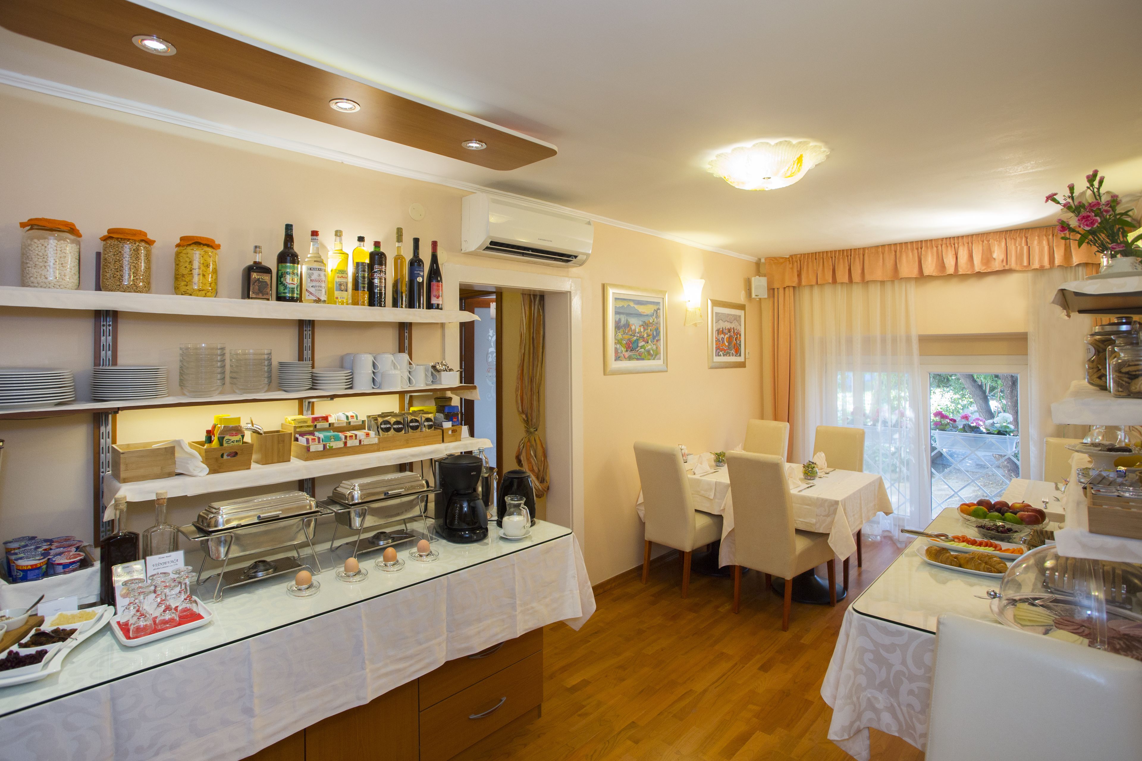 A breakfast buffet with various food items and beverages, a dining area with chairs and a table, and a window with curtains.