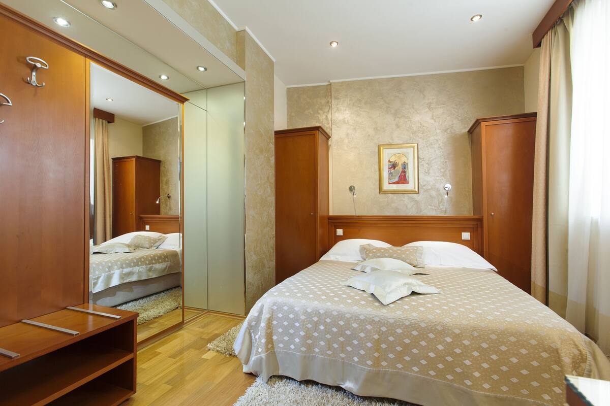Une chambre d’hôtel avec un grand lit, une armoire en bois, un miroir et un tableau au mur.