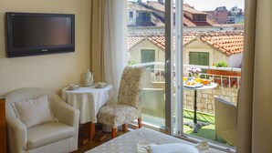 Habitación de hotel con cama, una silla, una mesita con tetera y un balcón con mesa y sillas.