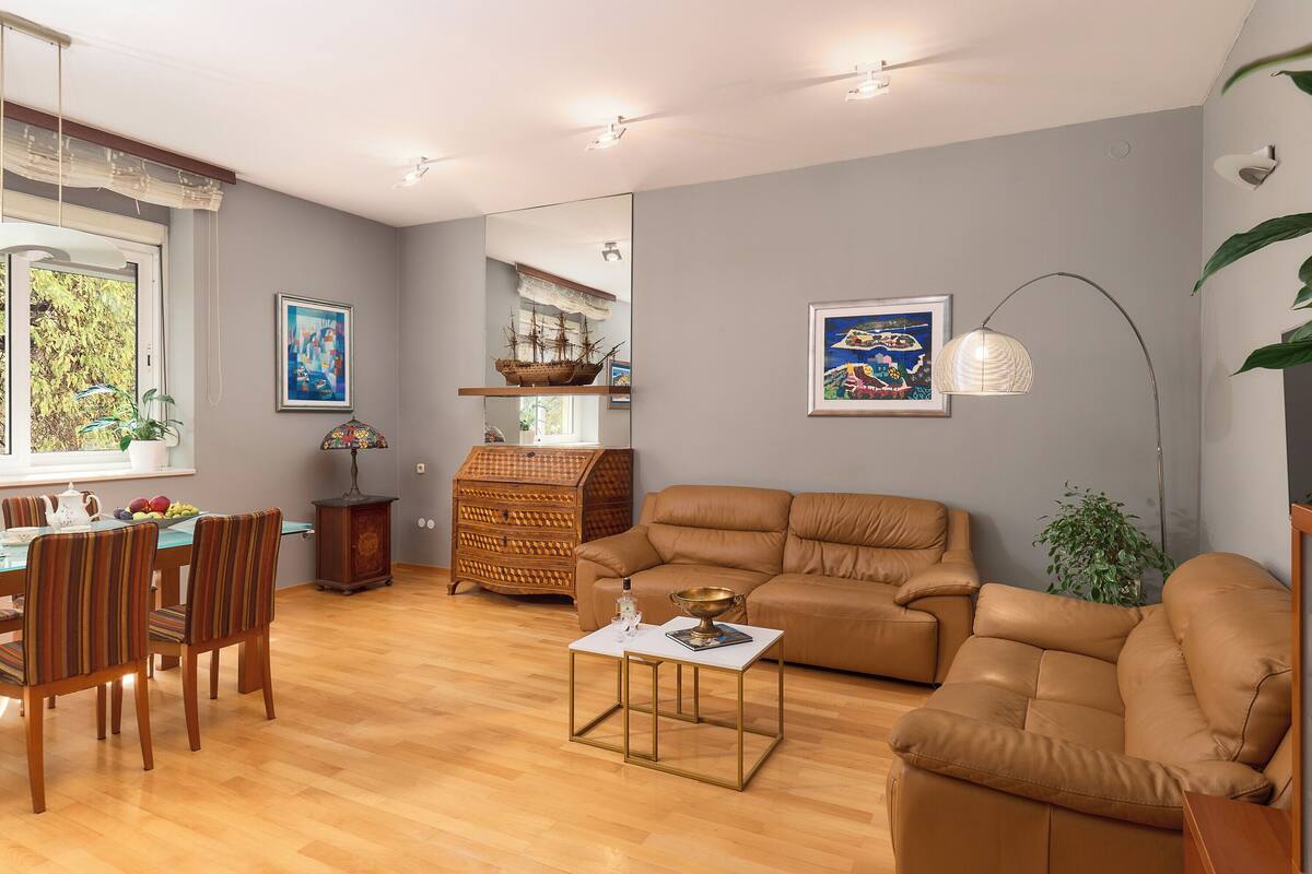 Un salon avec un canapé en cuir marron, une table à manger avec des chaises, une petite table basse blanche et une maquette de bateau posée sur une étagère.