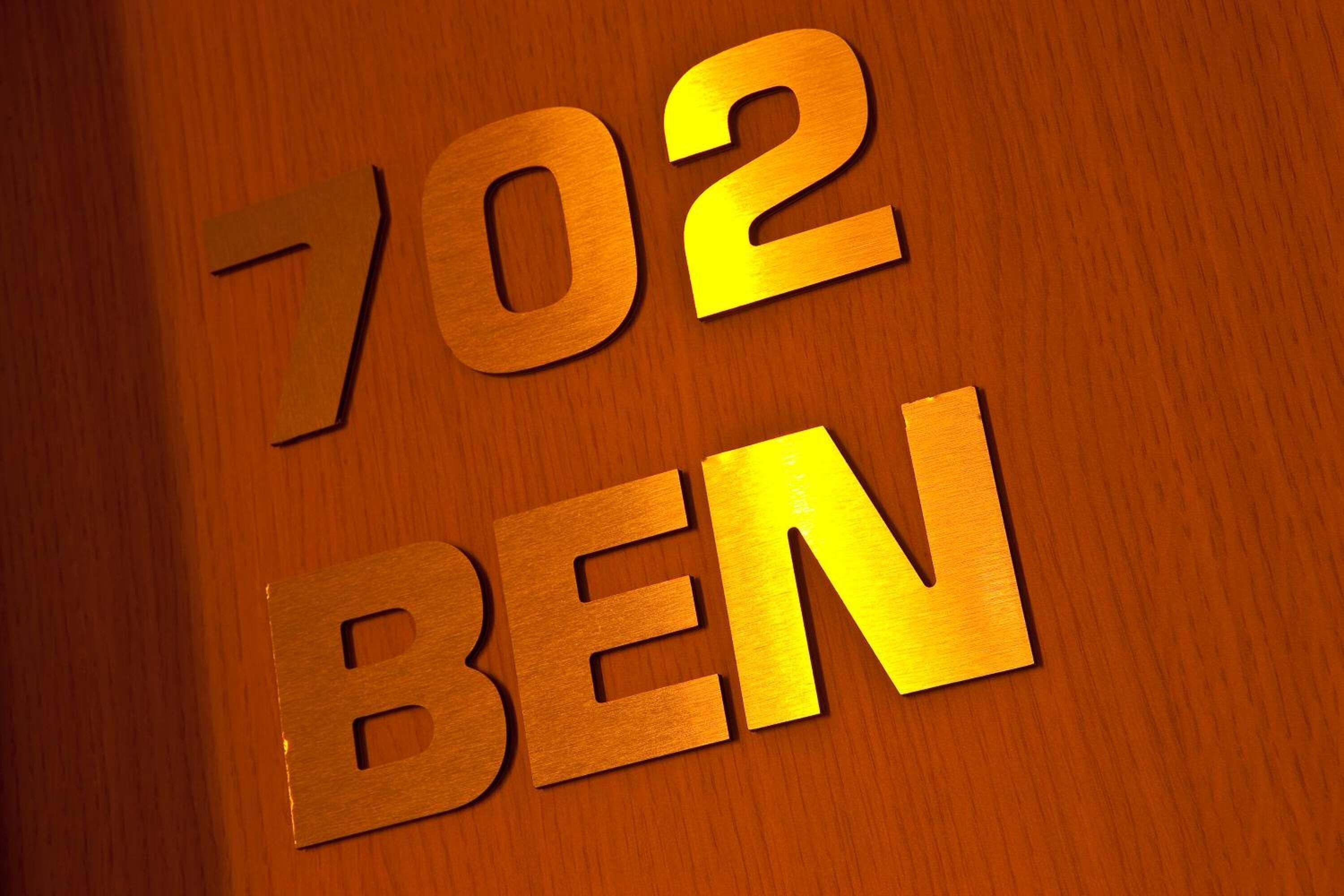 Pared de madera con los números "702" y las letras "BEN" en una tipografía dorada y llamativa.