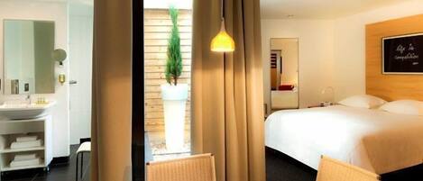 A hotel room with a bed, a bedside table, a mirror, a sink, and a window with curtains.