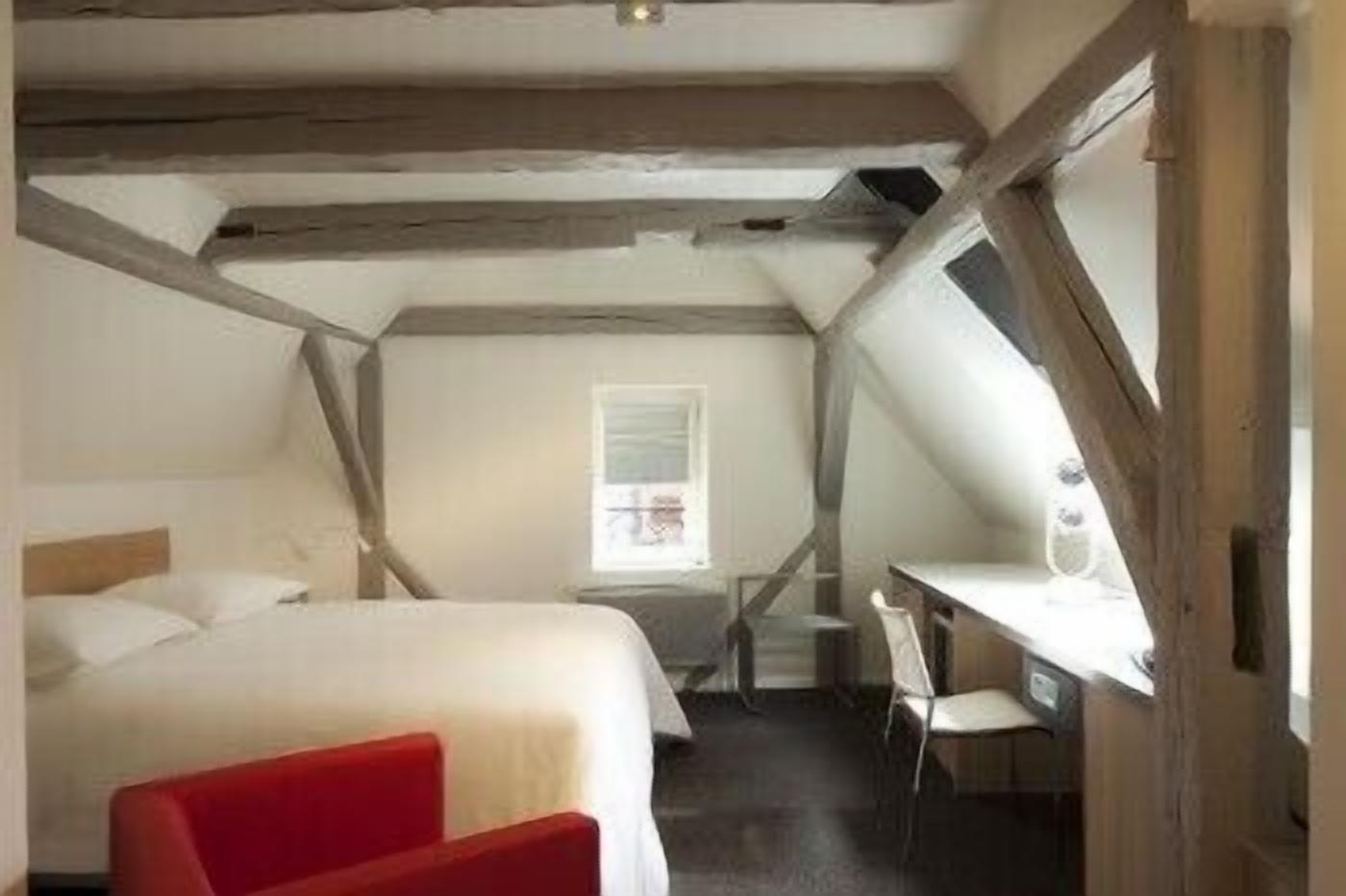 A bedroom with a bed, a desk, and a chair. There is a window with a view of the outside.