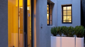 A building exterior with a glass door entrance, a window with a view, and a planter with shrubs.