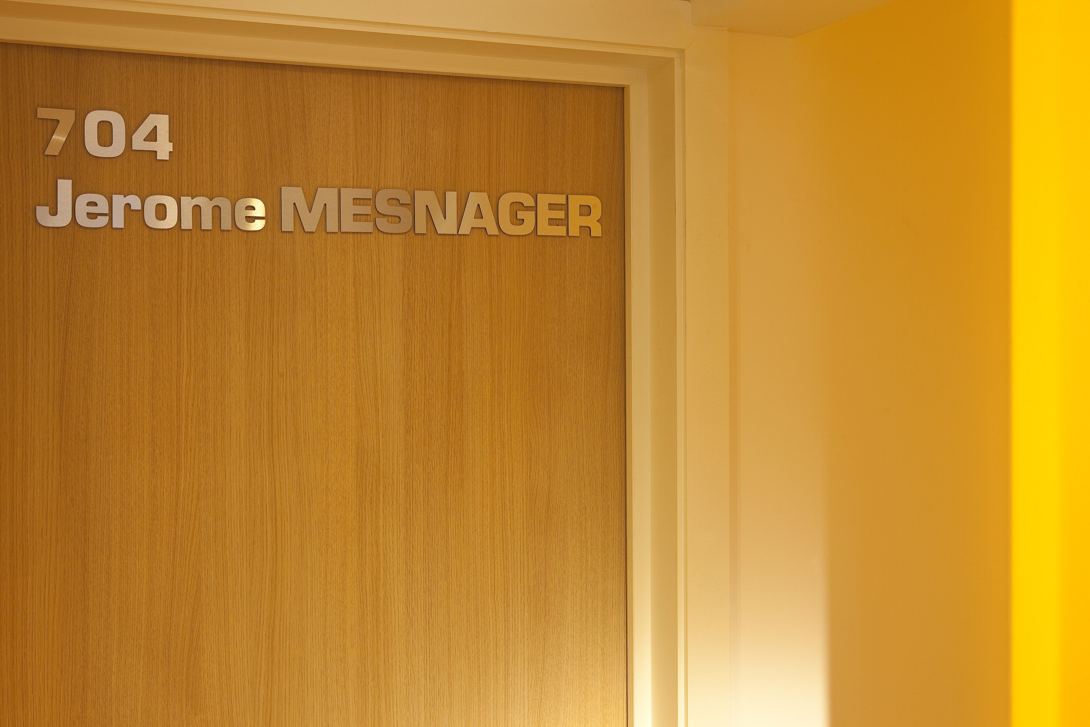 Una puerta de madera con el número 704 y el nombre 'Jerome MESNAGER' grabado.