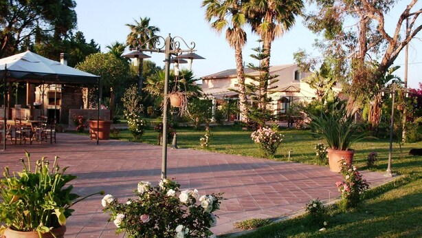 A patio area with outdoor seating, a pergola, and a garden with palm trees and potted plants. - Villa Cristina (Syracuse)